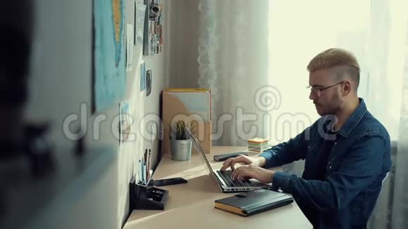 性格开朗的年轻男生带着眼镜和黄毛在家工作办公桌熟练的家庭自由职业者做笔记视频的预览图