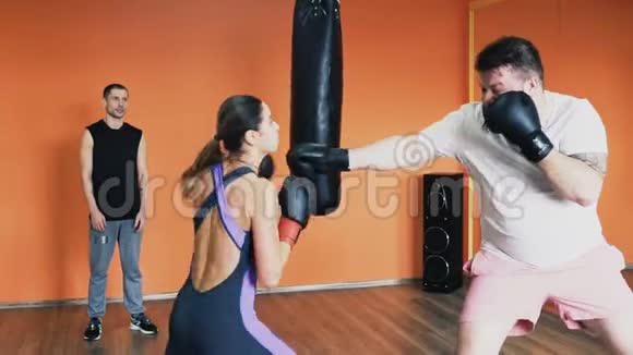 厚男人和苗条女人戴着拳击手套打架为胖子进行个人减肥训练个人培训视频的预览图