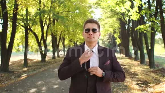 成功的商人西装革履地站在一个秋天的公园里系着领带视频的预览图