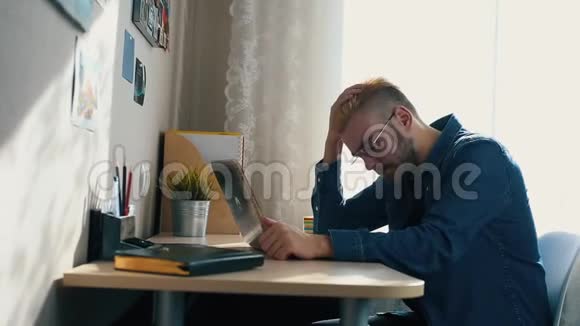 英俊的年轻家庭自由职业者戴眼镜黄头发在家工作使用笔记本电脑当收到坏消息时视频的预览图