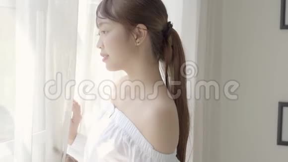 美丽的肖像年轻的亚洲女人早上醒来后在卧室里看窗外视频的预览图