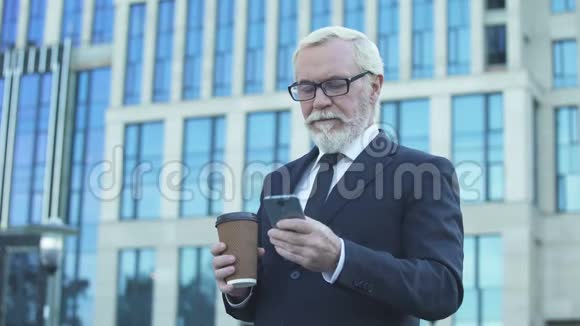高级商人在午餐时间喝咖啡在智能手机上滚动视频的预览图