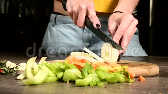 女性厨师的特写双手在切菜片旁边的木切割板上切洋葱的概念视频的预览图