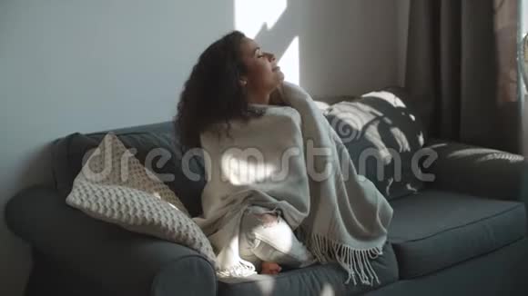 幸福美丽的女人坐在沙发上裹着毯子在家放松视频的预览图