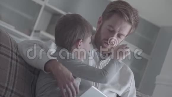 父亲和他的小儿子互相拉着鼻子坐在客厅的沙发上友好关系视频的预览图