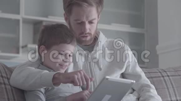 大胡子父子用数码平板电脑坐在休息室的沙发上幸福的家庭一起度过时光爸爸视频的预览图
