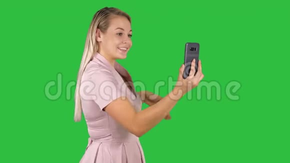 穿着粉红色裙子的女性用她的智能手机在绿色屏幕上打视频电话Chroma键视频的预览图