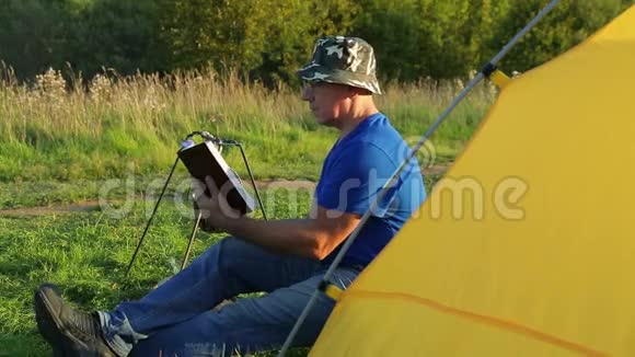 一个人在篝火帐篷附近看书看着沸腾的锅视频的预览图