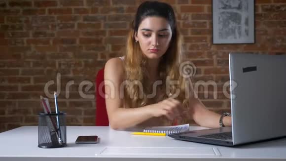 华丽的白种人女人坐在砖房里的笔记本电脑旁一边挂着电话视频的预览图