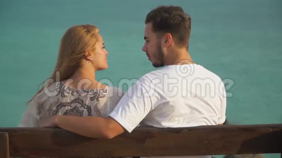 男人和女人坐在长凳上聊天大海在后面幸福的一对在户外共度时光闲暇时间视频的预览图