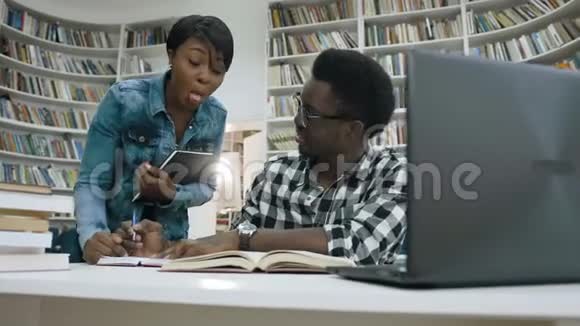 非洲女孩和男孩在学生图书馆准备考试时聊天和大笑视频的预览图