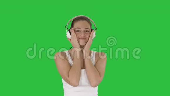 女人带着耳机听音乐在绿色屏幕上做滑稽的脸Chroma键视频的预览图