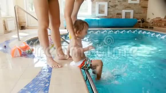 4k录像年轻母亲把她刚学会走路的儿子放在健身房的游泳池里视频的预览图