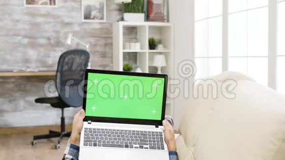 躺在沙发上拿着一台绿色屏幕笔记本电脑的人视频的预览图