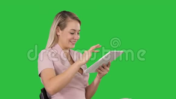女人坐着看平板电脑在绿色屏幕上微笑Chroma键视频的预览图