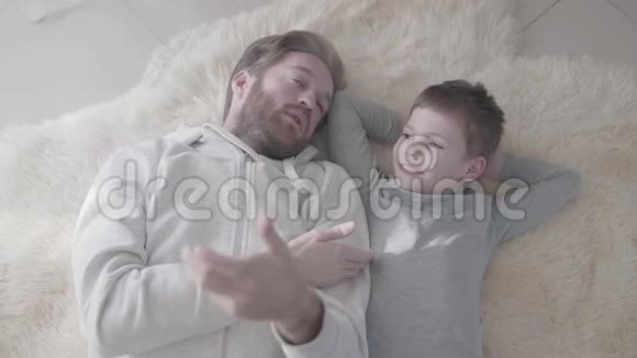 爸爸和他的儿子躺在毛皮地毯上用手势进行有趣的情感对话父亲和他说话视频的预览图