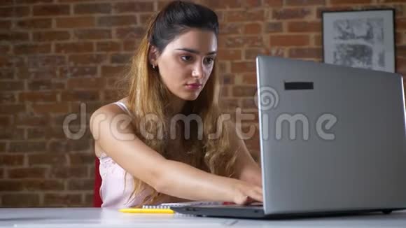 在红砖工作室里一个正在用笔记本电脑工作的白种人女孩疲惫地看着她并为放松而停下来视频的预览图