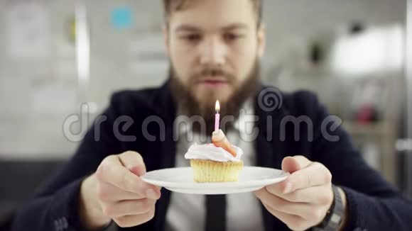 悲伤严肃的胡子商人办公室工作人员正在办公室里庆祝一个孤独的生日他正在吹蜡烛视频的预览图