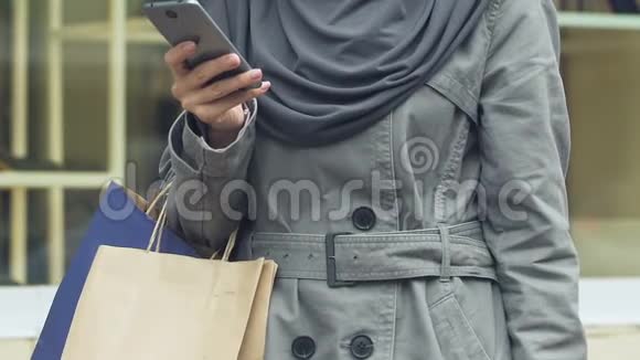 携带购物用品的穆斯林妇女购物后使用手机应用程序打出租车视频的预览图