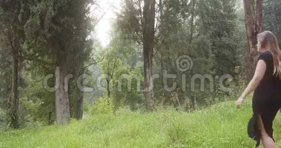 穿着黑色裙子走在绿色森林里的年轻美女视频的预览图