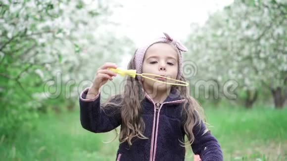 快乐的小女孩在春天公园吹肥皂泡慢动作视频的预览图