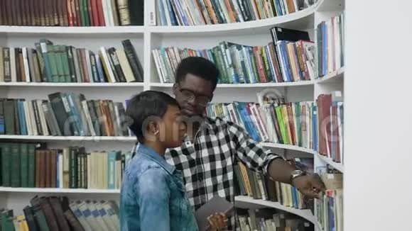 非洲男学生帮助从书架上挑选书籍给大学图书馆的另一名女学生视频的预览图