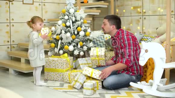 小女孩和爸爸在家中的圣诞树附近摇礼盒视频的预览图
