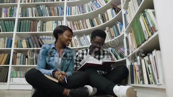 非洲男女学生看书准备考试坐在书架旁边的地板上视频的预览图