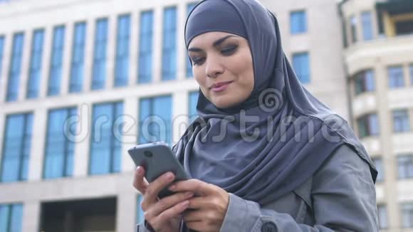使用智能手机的漂亮穆斯林女性在阅读留言后带着好消息微笑视频的预览图