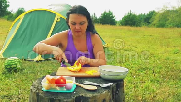 帐篷附近的一个女人用一把小刀在木板上用小方块削着黄色的辣椒视频的预览图