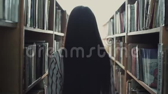 一位美丽的年轻女子走在图书馆的书架之间概念教育视频的预览图