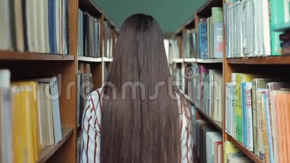 一位美丽的年轻女子走在图书馆的书架之间概念教育视频的预览图