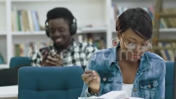 吸引人的非洲女学生在现代图书馆看书而非洲男学生在使用智能手机视频的预览图