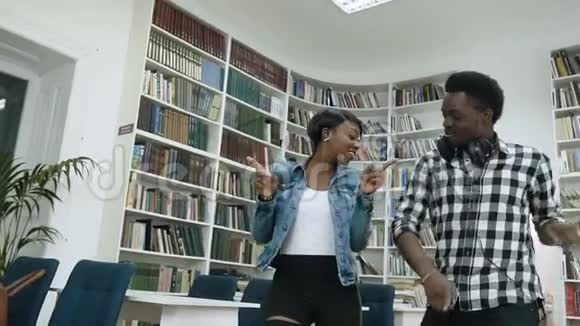 一对非洲男女学生边听音乐边在现代图书馆跳舞视频的预览图