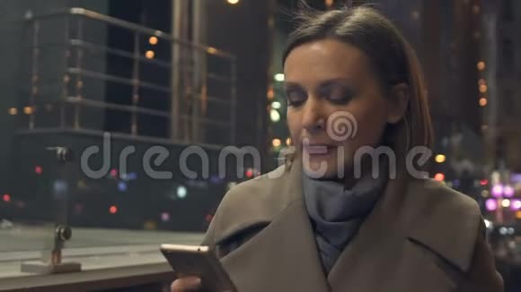 漂亮的女性在晚上用手拿着智能手机走路看电子邮件视频的预览图