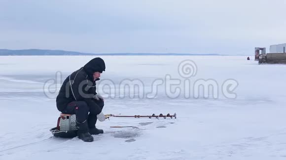 渔夫坐在冰冻的河边钓鱼然后把冬天的鱼竿放在冰上从热水瓶里倒热茶视频的预览图