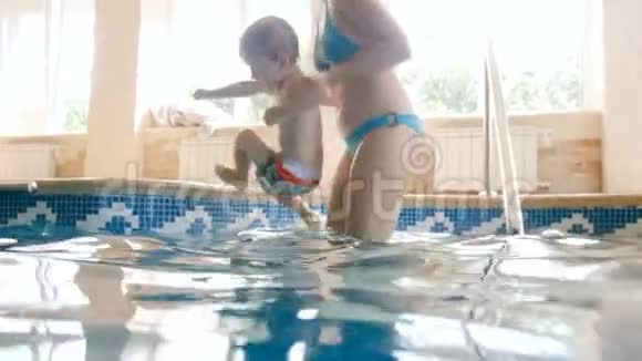4k慢速动作镜头快乐微笑的母亲抱着孩子在游泳池里吐气视频的预览图