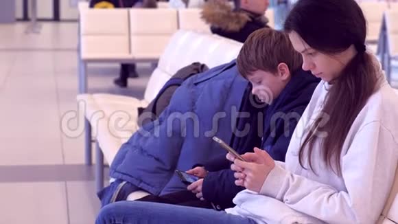 女伴儿子在机场大厅手机上浏览等待航班侧视视频的预览图