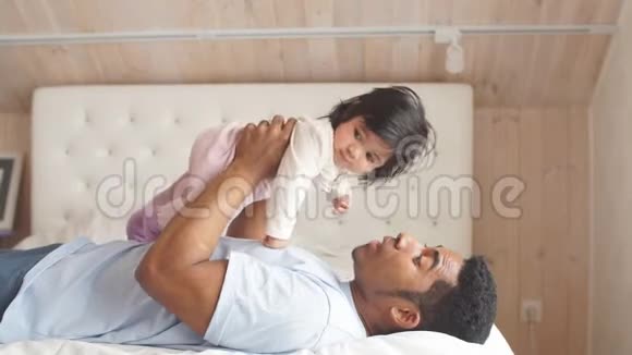 嬉戏的父亲扶着小女儿躺在床上视频的预览图