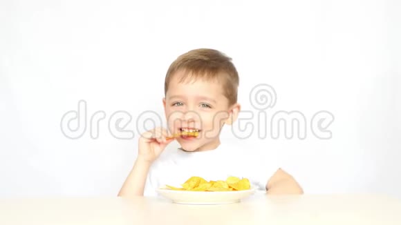 一个快乐和快乐的孩子在白色背景的桌子旁坐着吃薯片然后举起大拇指视频的预览图