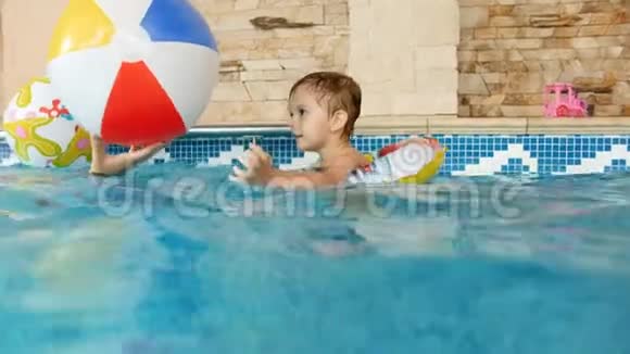 4k视频快乐妈妈带孩子在室内游泳池玩充气彩色沙滩球视频的预览图