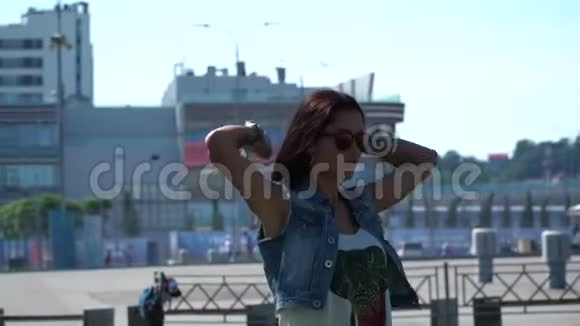 身着纹身自信的黑发女士在城市建筑前戴上现代耳机视频的预览图