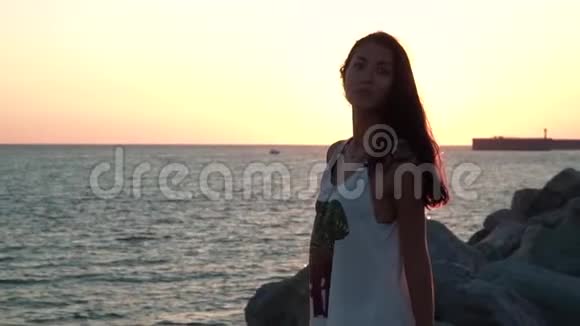 日落时分在海滩上慢动作摆姿势的美丽女孩的肖像视频的预览图