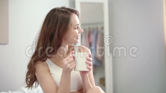 年轻女子在床上享受早晨的咖啡幸福女人的画像视频的预览图