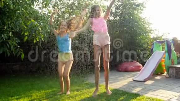 阳光明媚的一天欢快的少女们在花园水管里的水滴下嬉戏视频的预览图