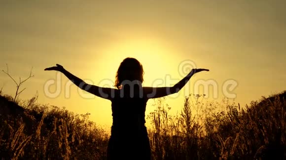一个女人的轮廓她沉思着阳光明媚的夕阳背景双手在头顶上方视频的预览图