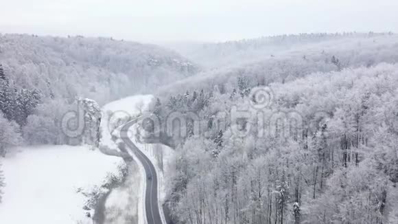 鸟瞰一个美丽的冬季景观一辆汽车沿着一条道路在一个覆盖着雪的森林冬天视频的预览图