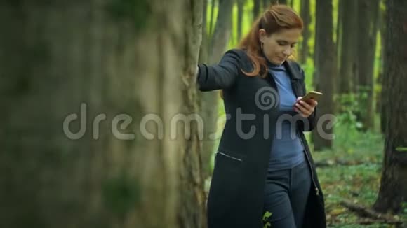 女孩站在树旁边在电话里写短信视频的预览图
