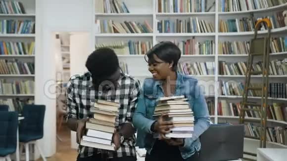 年轻的非洲夫妇手里拿着一堆书一边在图书馆的背景上谈笑风生视频的预览图
