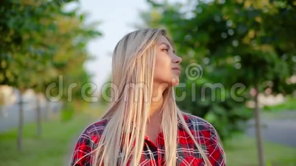 一位美丽的金发女孩穿着红色格子衬衫站在小巷里微笑着视频的预览图